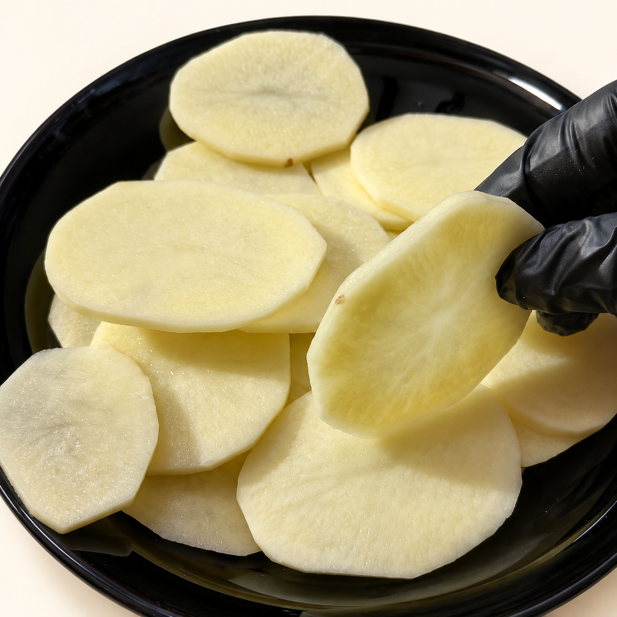 Rodajas frescas de papa española sobre plato negro, con una rodaja sostenida con guante para mostrar el corte.