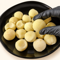 Papas noisette frescas sobre plato negro, con una pieza sostenida con guante para mostrar el corte.
