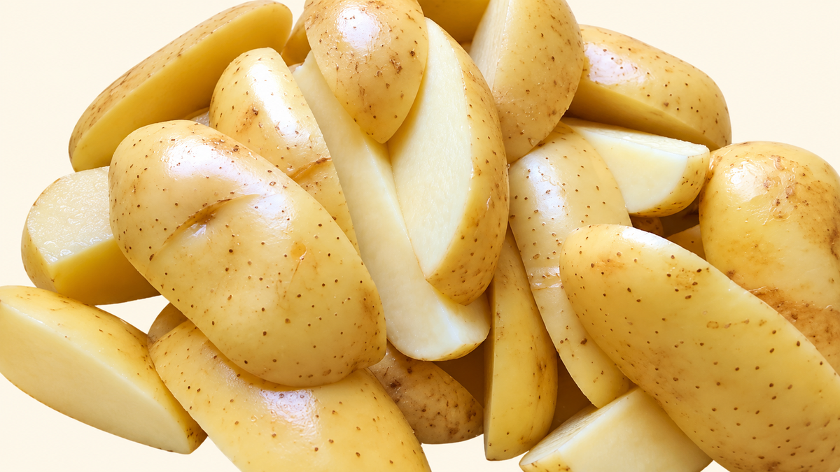 Detalle de papas rústicas frescas en cuñas con cáscara sobre fondo crema.