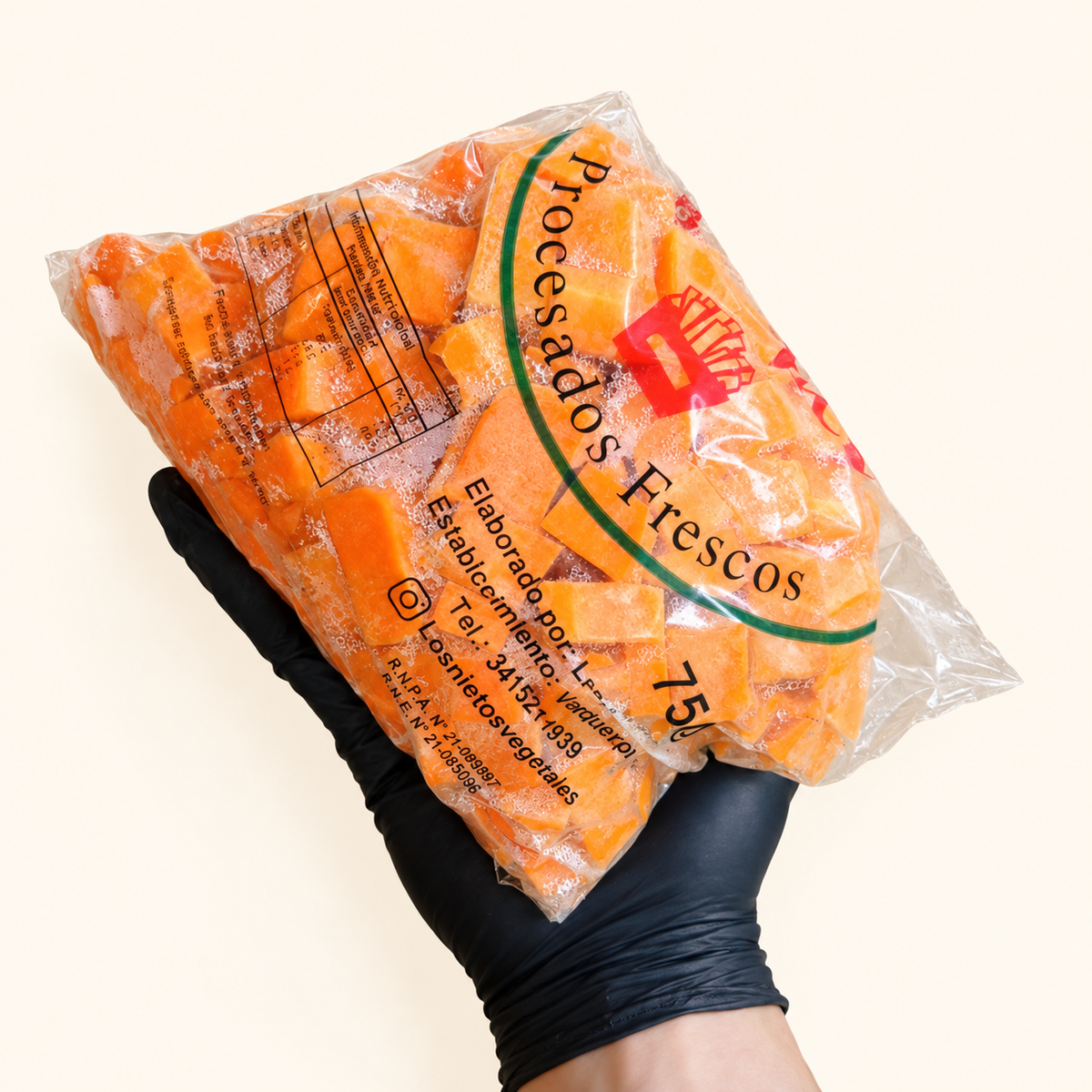 Zanahoria fresca en cubitos Los Nietos, envase de 750 g sostenido con guante sobre fondo crema.